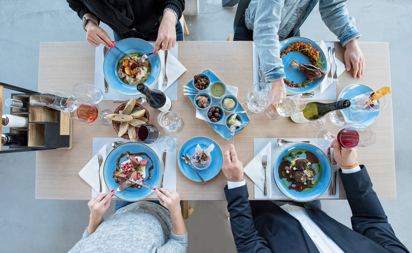 Restaurantbesuch aus der Vogelperspektive: Vier festlich gekleidete Personen an einem Tisch mit gehobenen Gerichten, einem Vorspeisenteller, Weingläsern, einer Flasche Etyeki Kúria Sauvignon Blanc 2022 und einer Flasche Etyeki Kúria Pinot Noir.